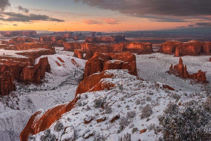 Snow-covered red rock formations at sunrise in Monument Valley.