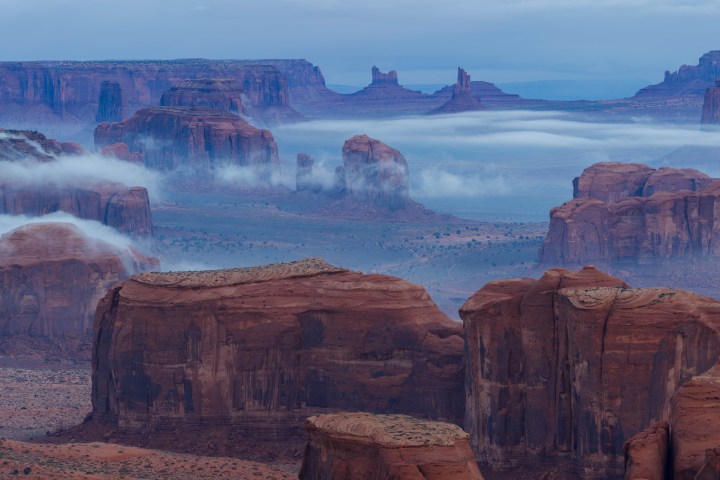 Foggy desert landscape with red rock formations and mesas.