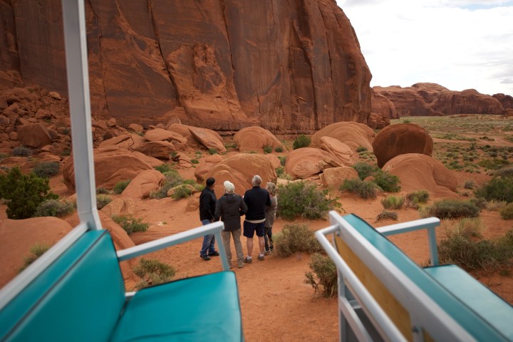 Three people at a rocky desert landscape near large red cliffs.