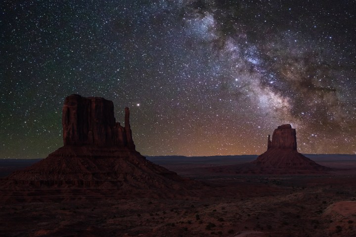 Starry night sky over desert with rock formations.